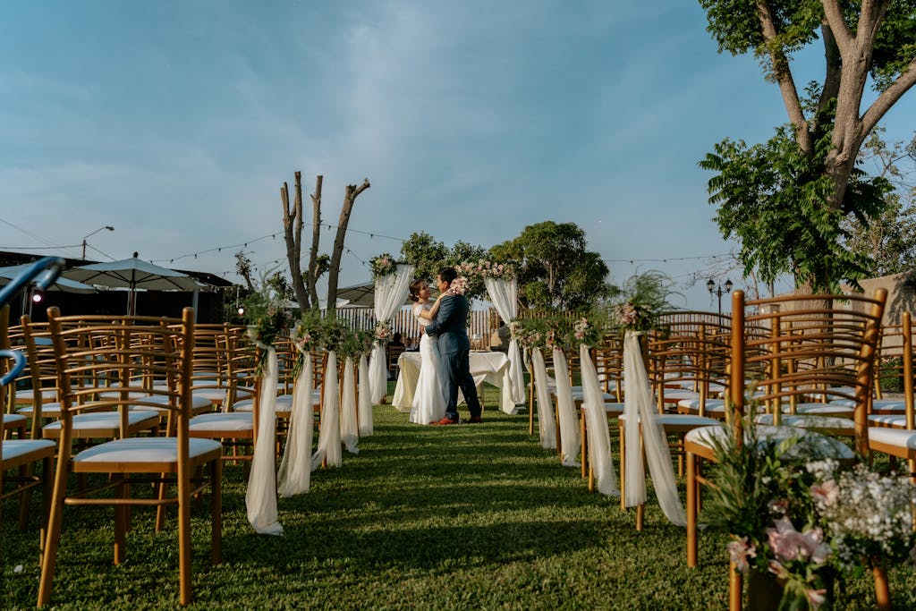 A romantic outdoor wedding setup featuring a couple embracing amidst decorated chairs and greenery.